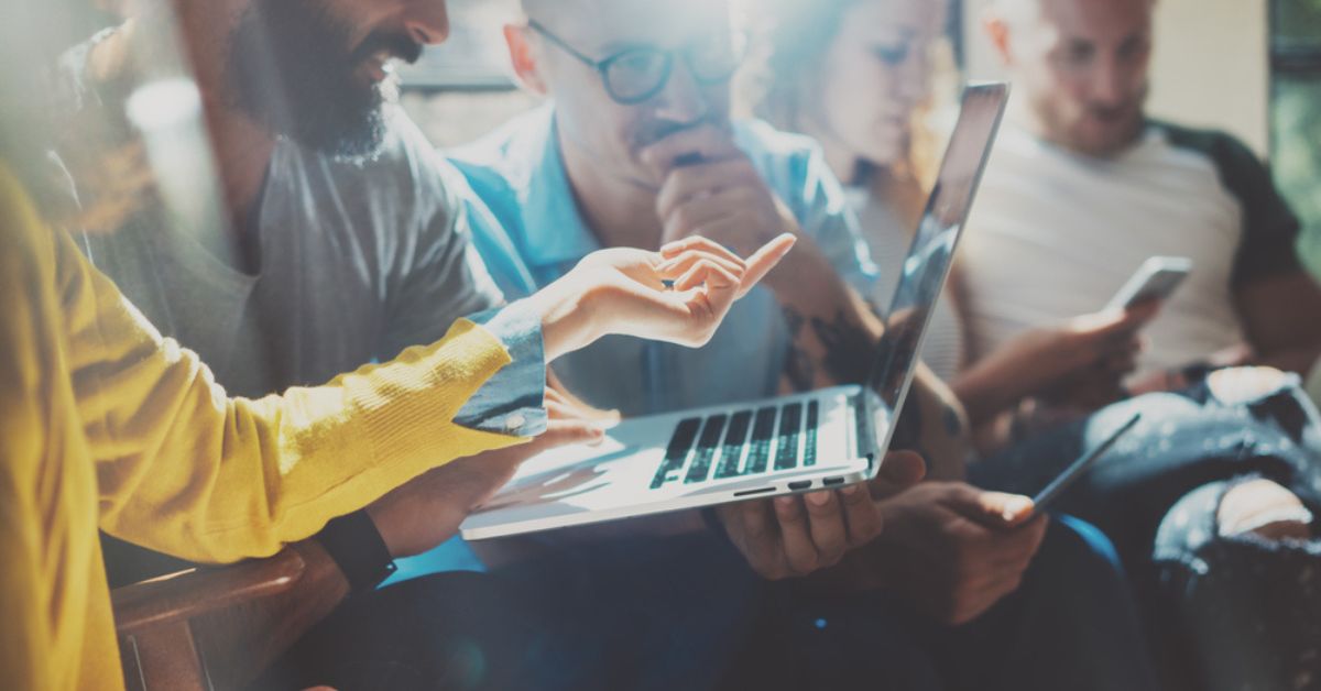 Hand pointing towards a laptop with other people in the background