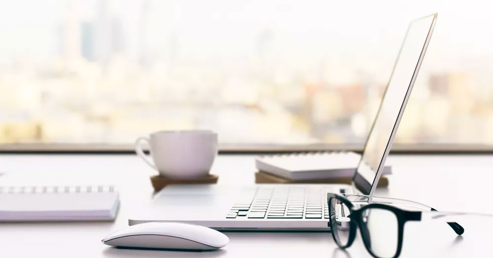 Tabletop with laptop, eyeglasses, notebooks, and coffee cup