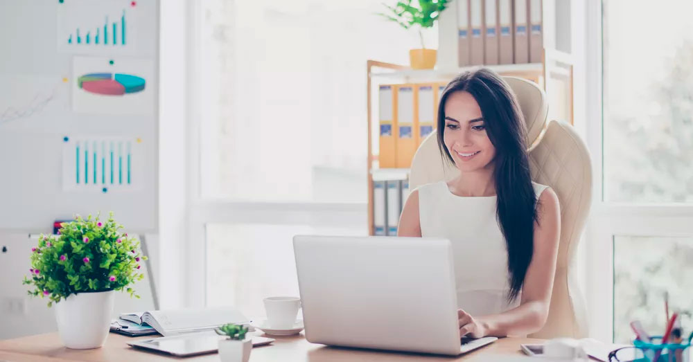 Woman typing on a laptop in a bright white office full of sunshine